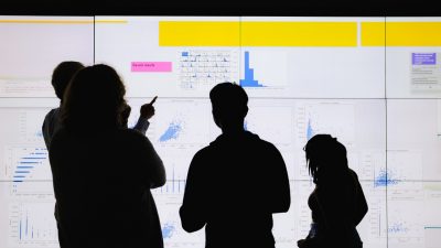Group of individuals in silhouette stand in front of data visualization screen.