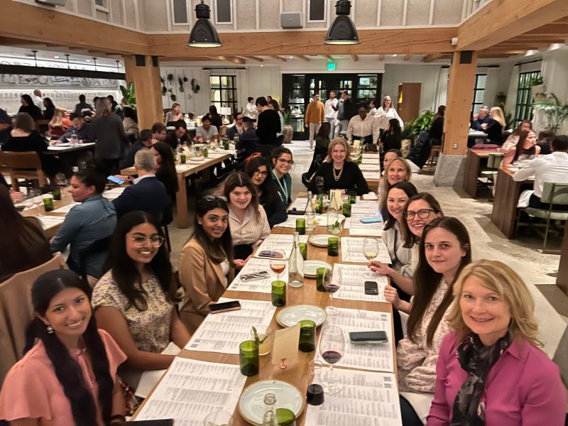 A group of 13 women gather around a dinner table.