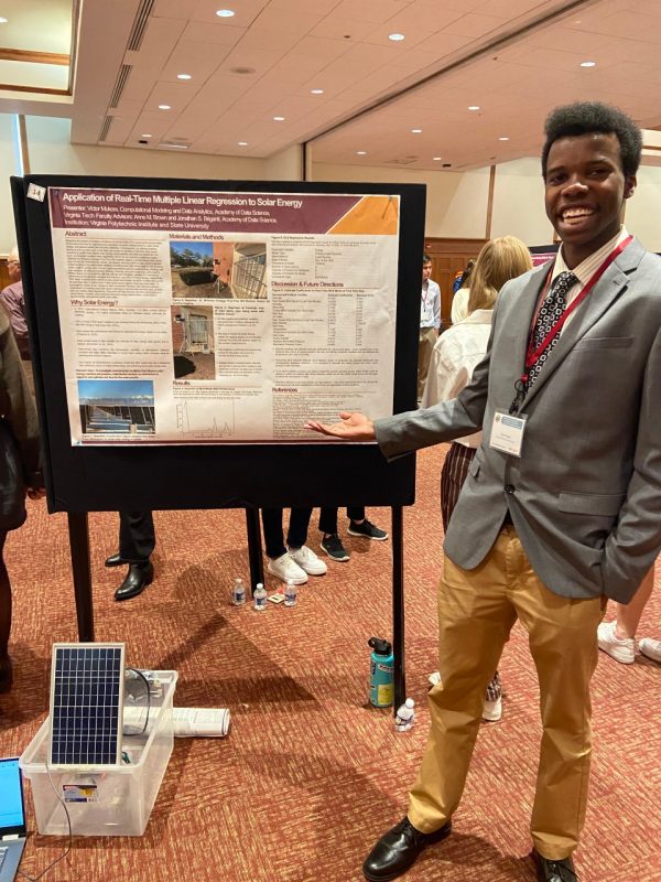 Victor Mukora stands to his research poster and solar panel.