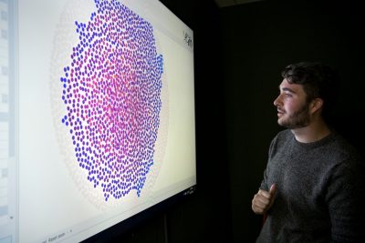 man looks to left at projection with a cluster of purple dots in a heat map