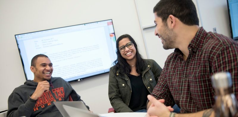 2 male and 1 female student laugh while sitting around a classroom table