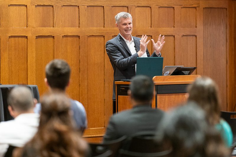 Keith Johnson stands at a podium and gestures with his hands while speaking in front of an audience.